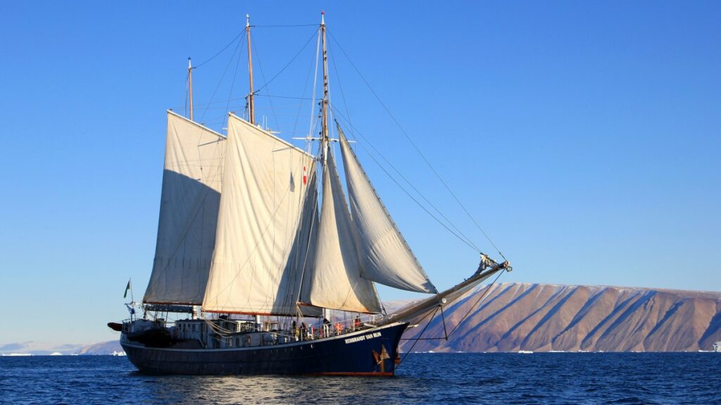 A ship at full sail crossing calm waters during a blue sky day.