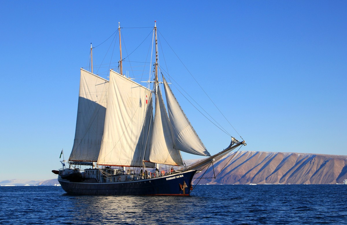 A ship at full sail crossing calm waters during a blue sky day.